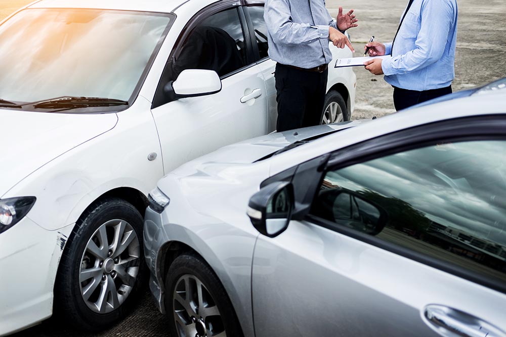 Insurance agent writing on clipboard while examining car after a