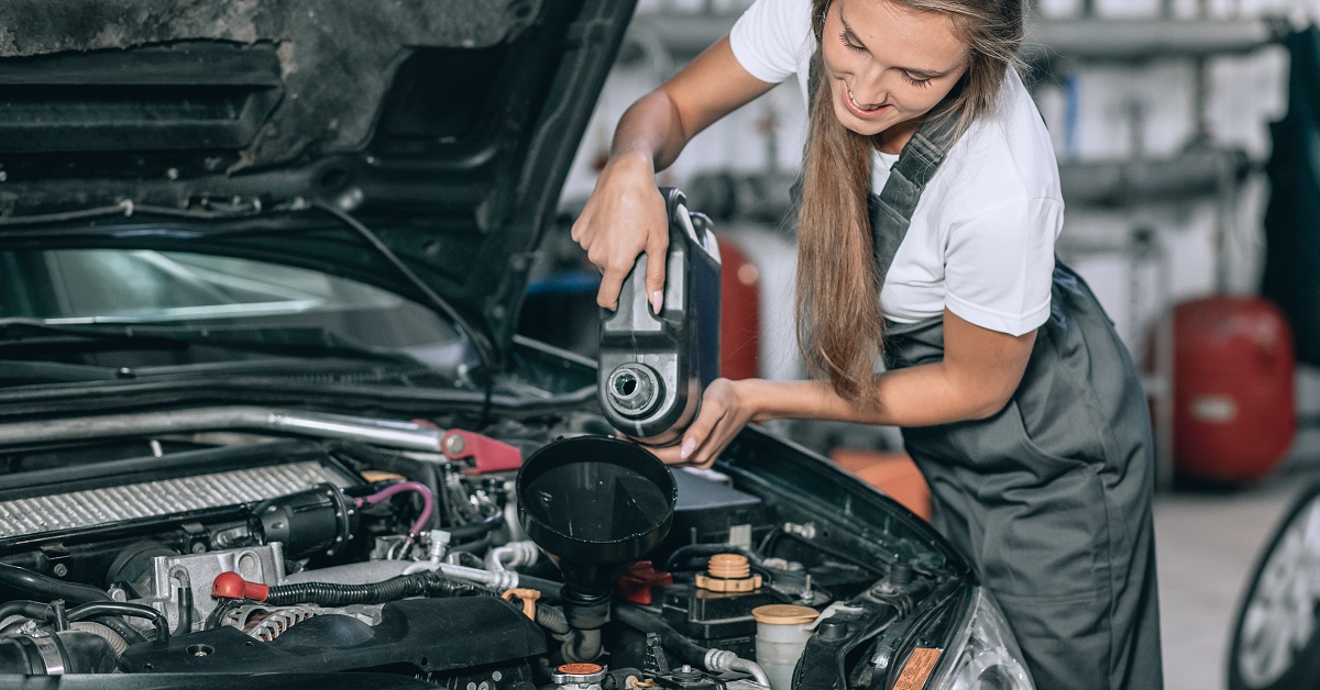 Beautiful Mechanic girl in a black jumpsuit and a white T shirt changes the oil in a black car