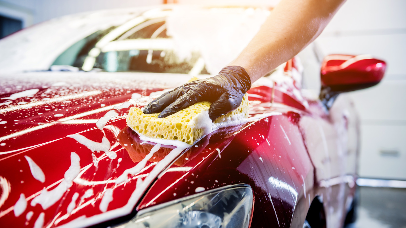 Worker washing red car with sponge on a car wash