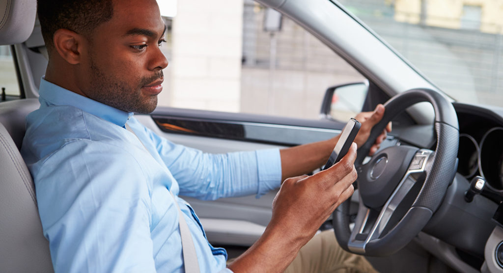 Young African American male driver using phone, in car view