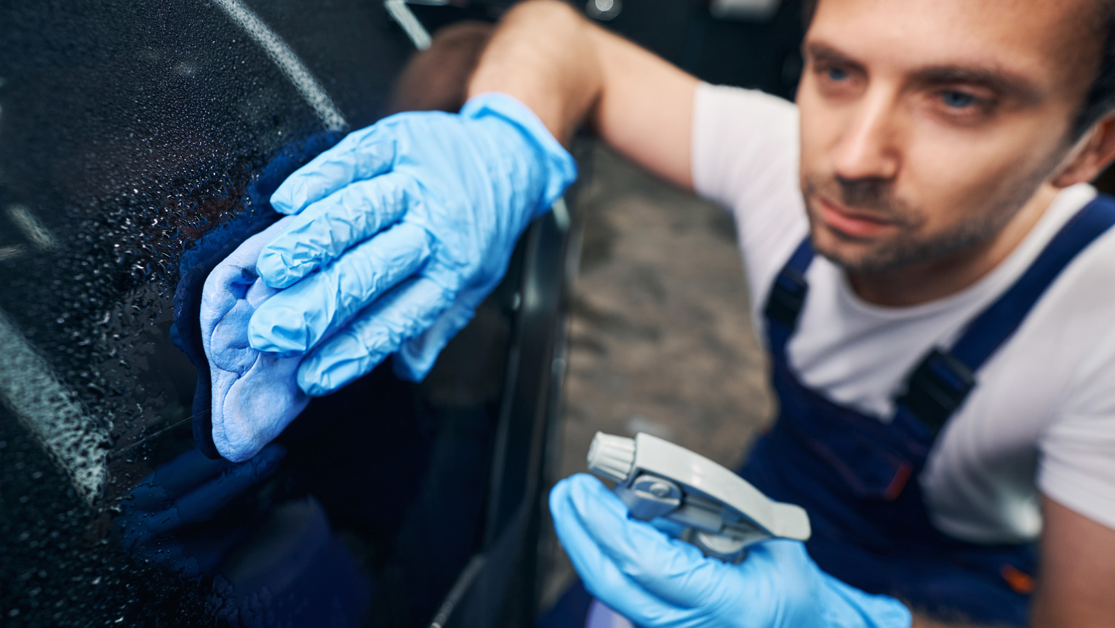 A mechanic cleaning a car surface with a degreaser spray