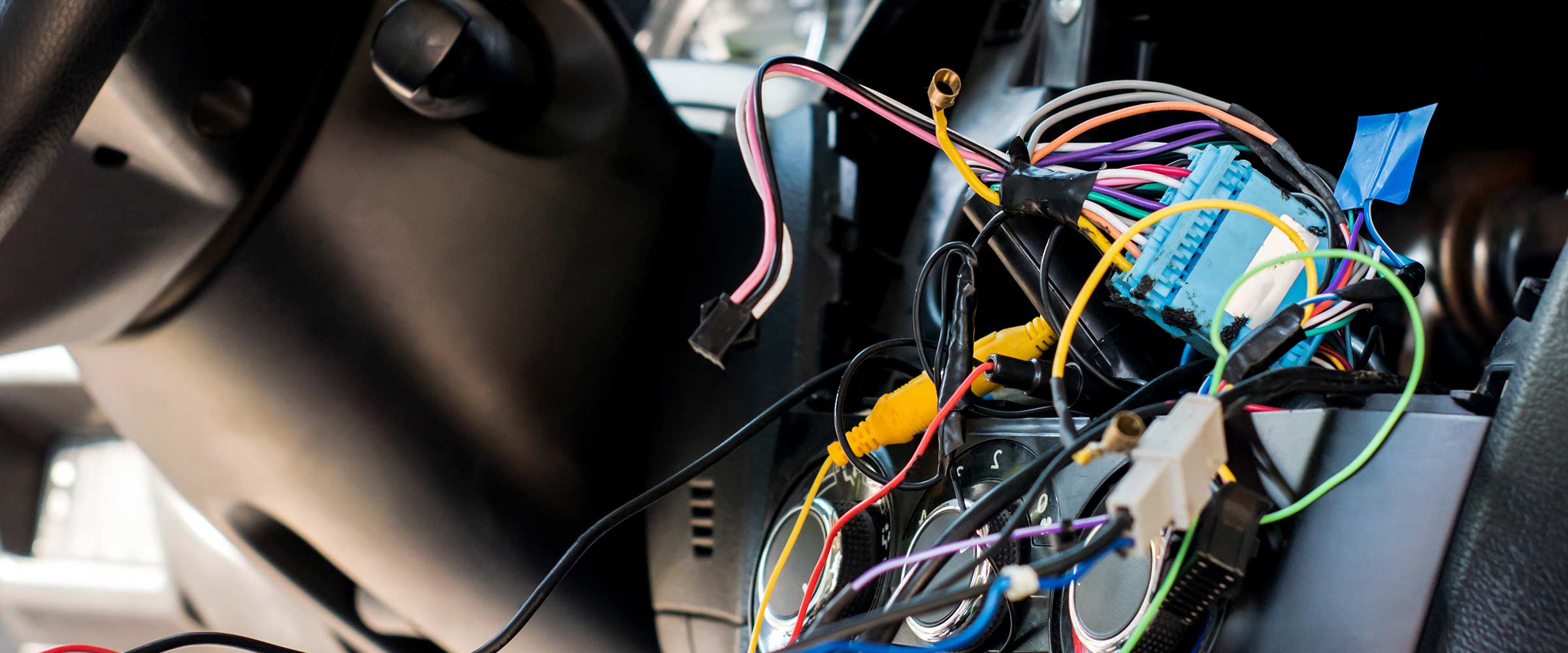 A complicated wiring harness and electrical connectors are located behind a car's dashboard