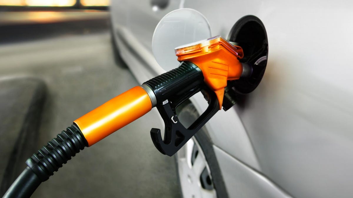 Fuel nozzle being used to fill a silver car at a gas station