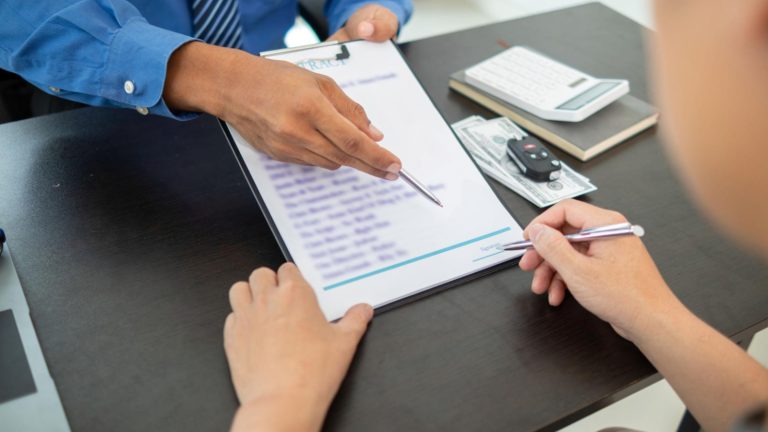 A professional pointing at a contract while a person prepares to sign