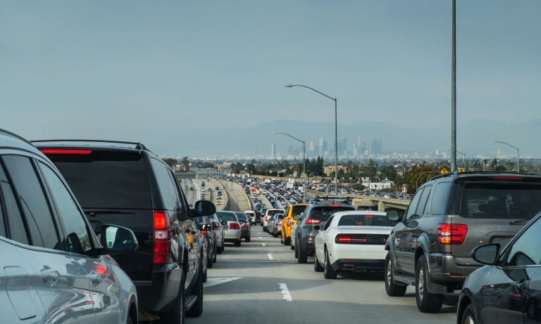 Heavy traffic of cars moving slowly along a multi-lane freeway with distant city skyline views