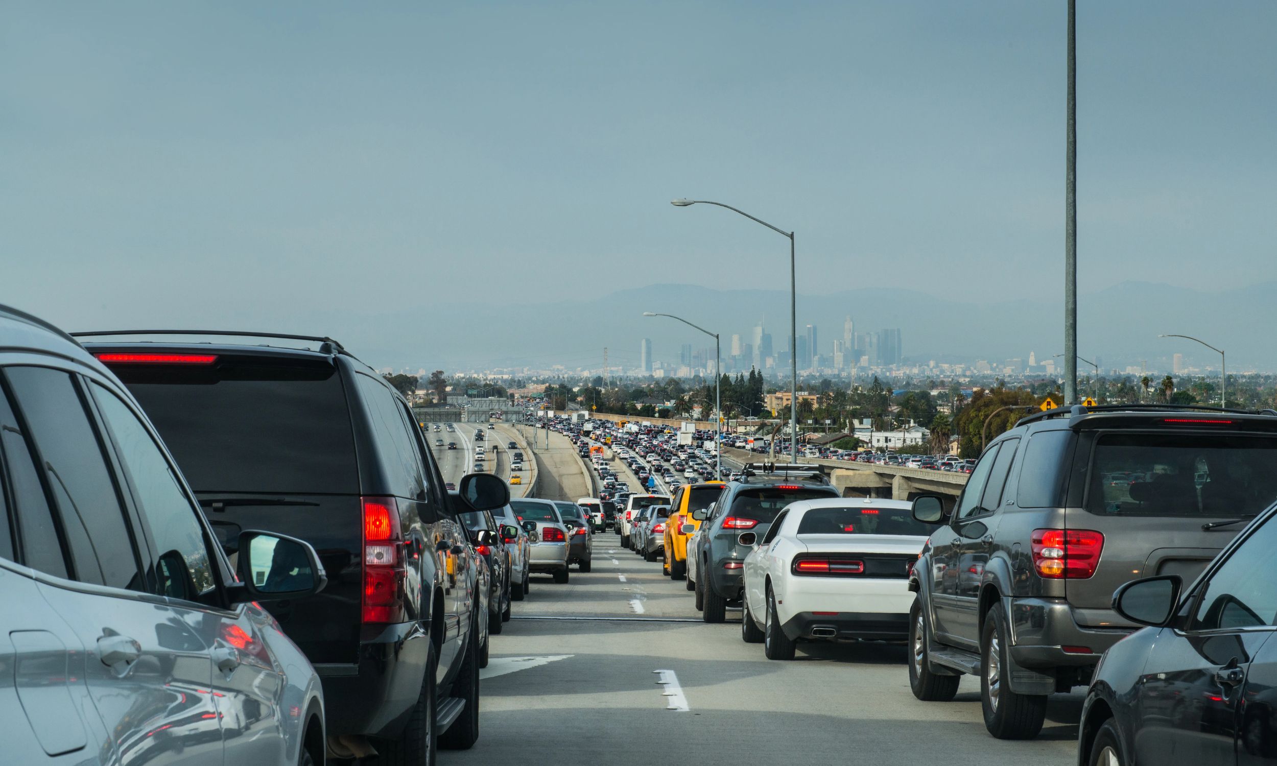 Heavy traffic of cars moving slowly along a multi-lane freeway with distant city skyline views