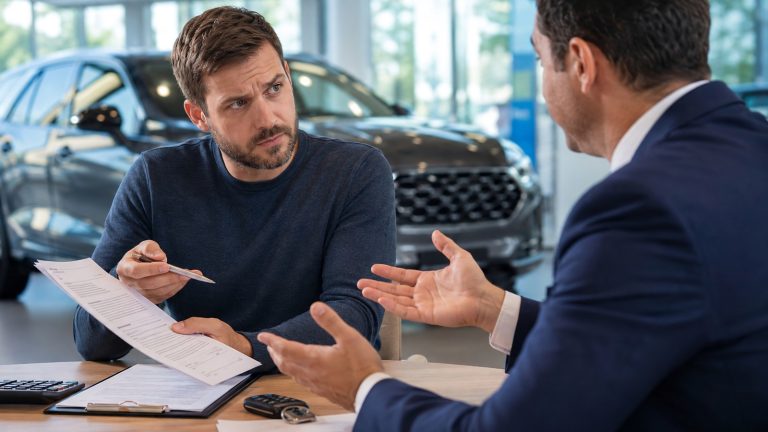 A skeptical car buyer holding a pen and contract talking with a car salesman