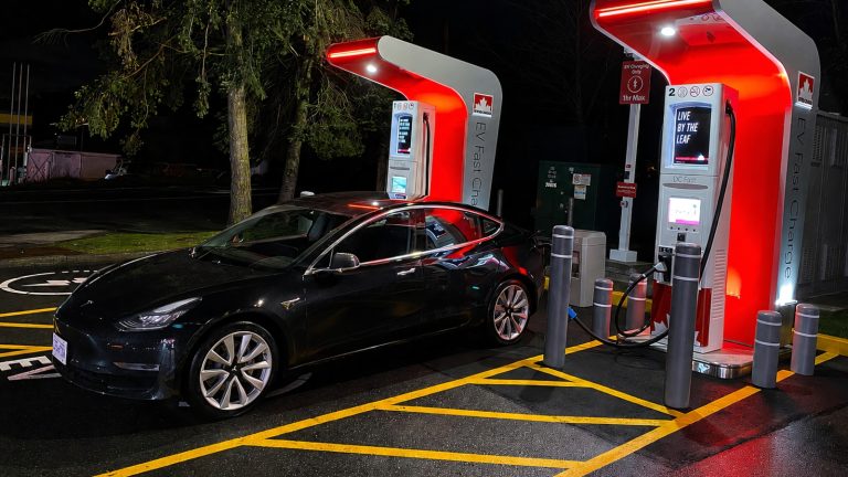 black electric car parked at a brightly lit charging station at night