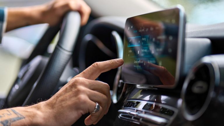 Driver using a finger to tap the dashboard touchscreen display inside a modern vehicle