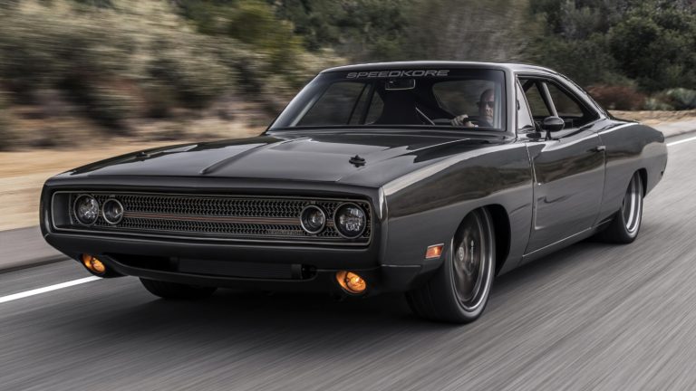 A sleek dark vintage muscle car driving fast along a paved winding road