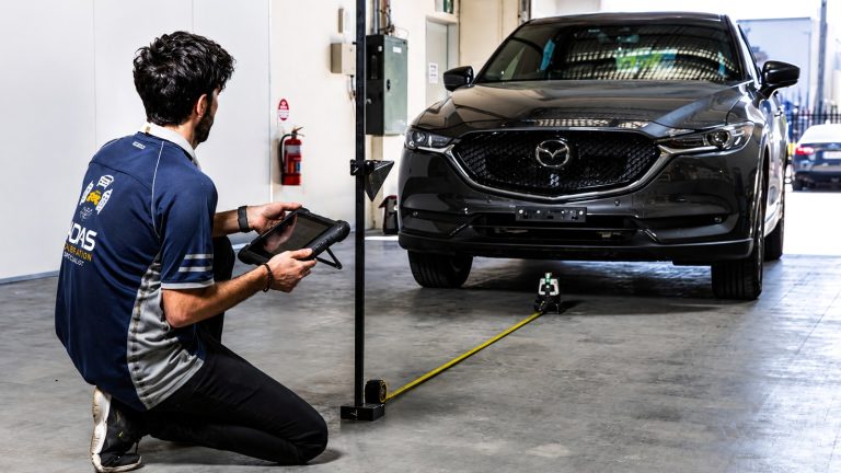 technician kneels in a garage, using a tablet to calibrate a dark SUV's ADAS sensors