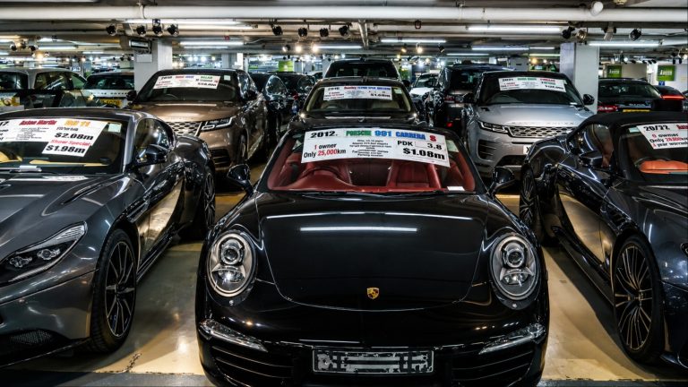 An indoor underground parking garage filled with various luxury cars for sale with price tags