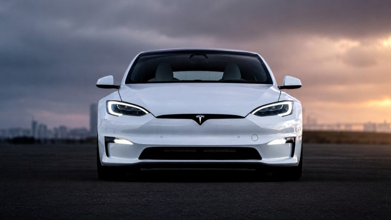 Front view of a modern white electric car parked against a cloudy sunset sky