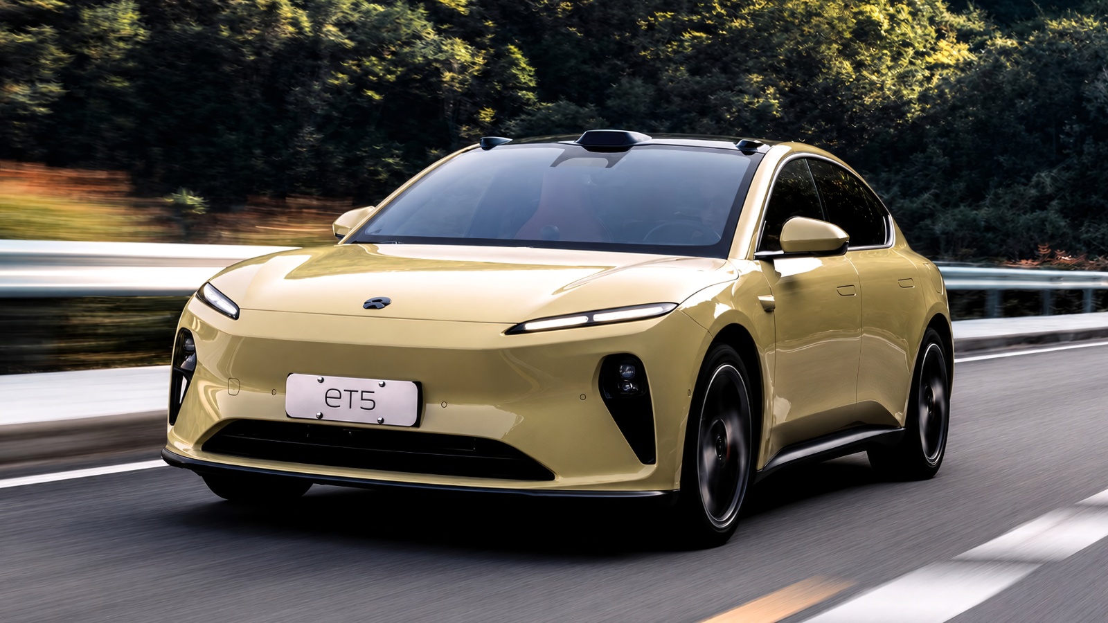 yellow electric sedan driving on a paved road surrounded by green trees