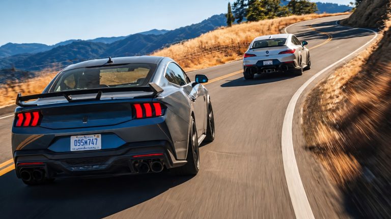 Two modern sports cars driving on a winding asphalt mountain road surrounded by dry hills