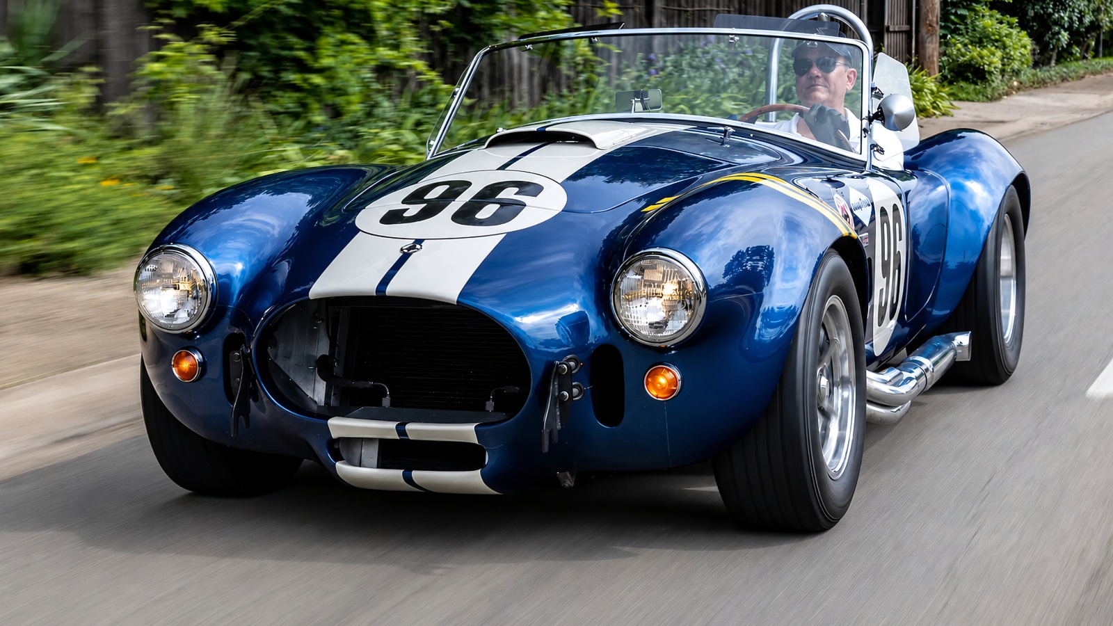 blue and white Shelby Cobra racing car drives along a sunlit street