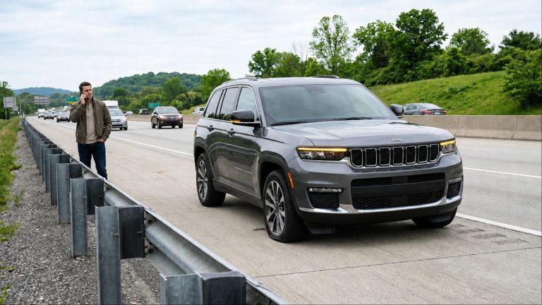 Driver standing beside a stalled SUV on the highway shoulder making a phone call