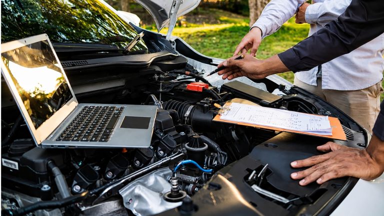 Mechanics inspecting a car engine bay with a laptop and a checklist clipboard