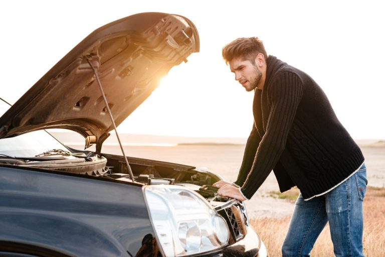 Young upset casual man trying to fix his broken car outdoors
