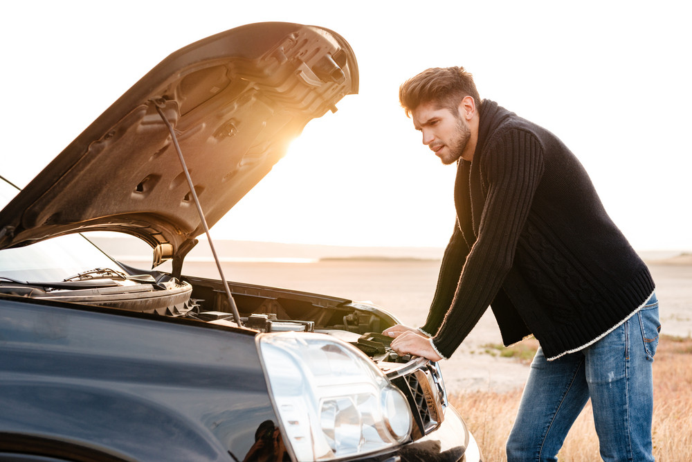 Young upset casual man trying to fix his broken car outdoors