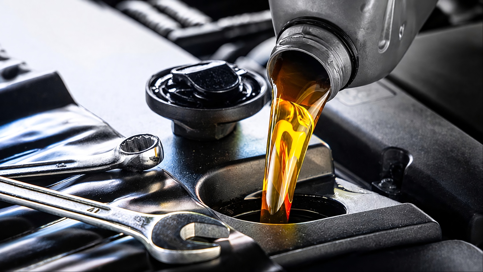 Golden motor oil pours into a car engine with wrenches