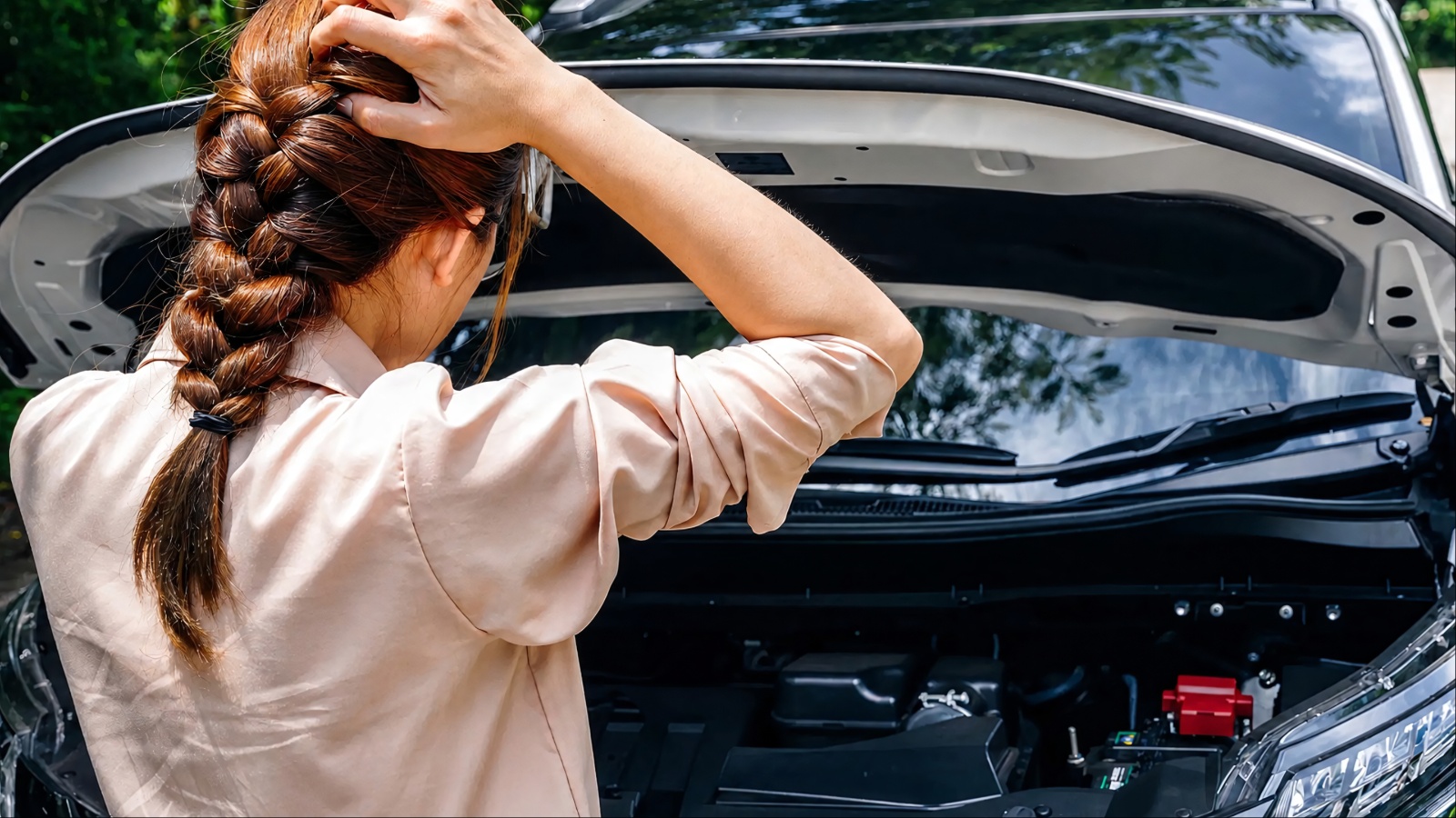 Frustrated person looking at a car engine with the hood open