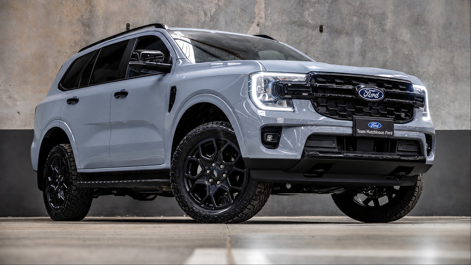 modern grey Ford Everest SUV with black alloy wheels parked against a concrete textured wall