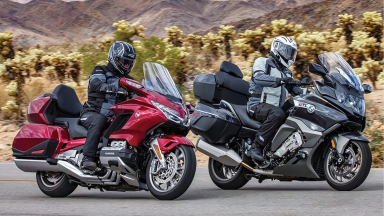 Two motorcyclists ride touring bikes along a desert highway with hills