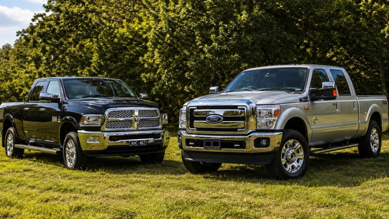 dark pickup truck and a silver pickup truck parked outdoors on grassy ground