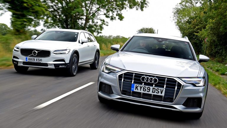 Two modern station wagons, a white Volvo and a silver Audi, driving on a road