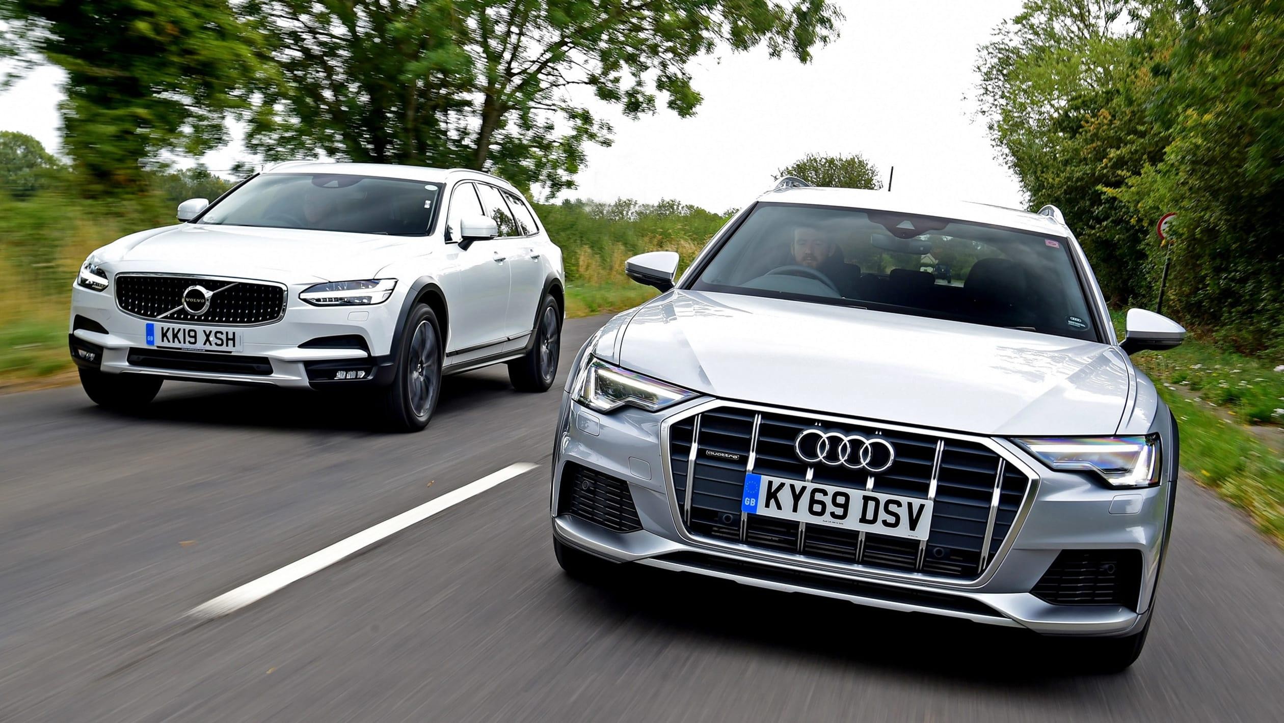 Two modern station wagons, a white Volvo and a silver Audi, driving on a road