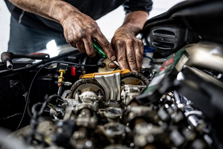 mechanic with greasy hands uses a screwdriver inside a detailed car engine bay