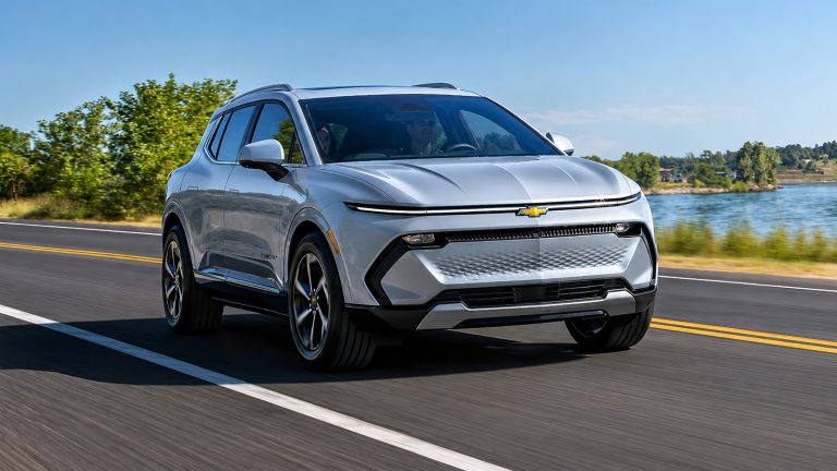 silver Chevrolet electric SUV driving on a scenic coastal highway under clear skies.