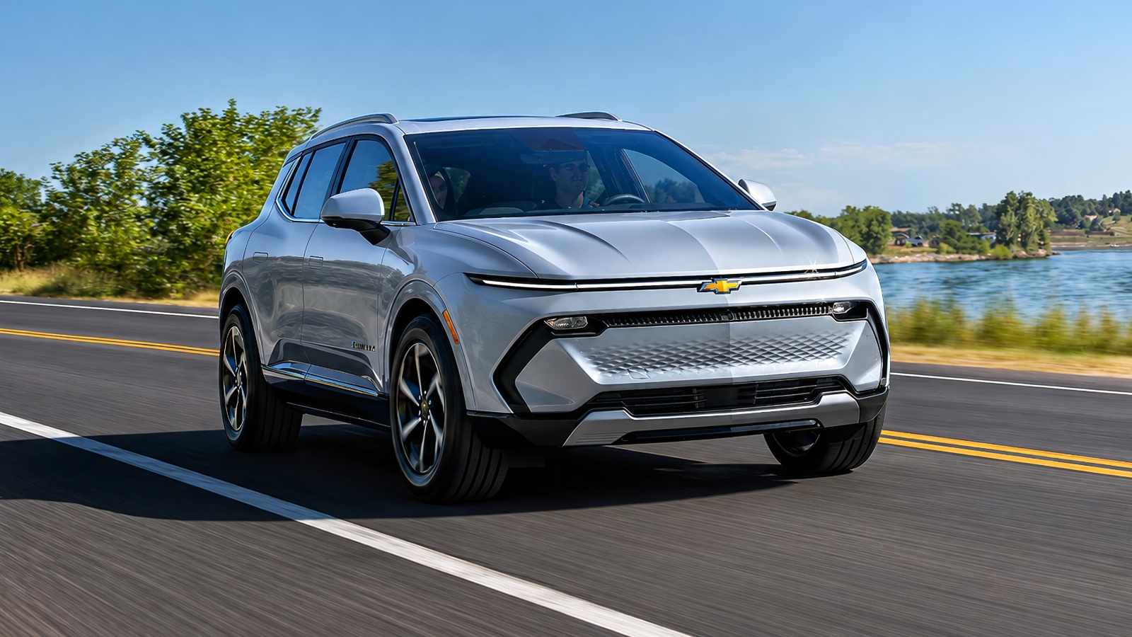 silver Chevrolet electric SUV driving on a scenic coastal highway under clear skies.
