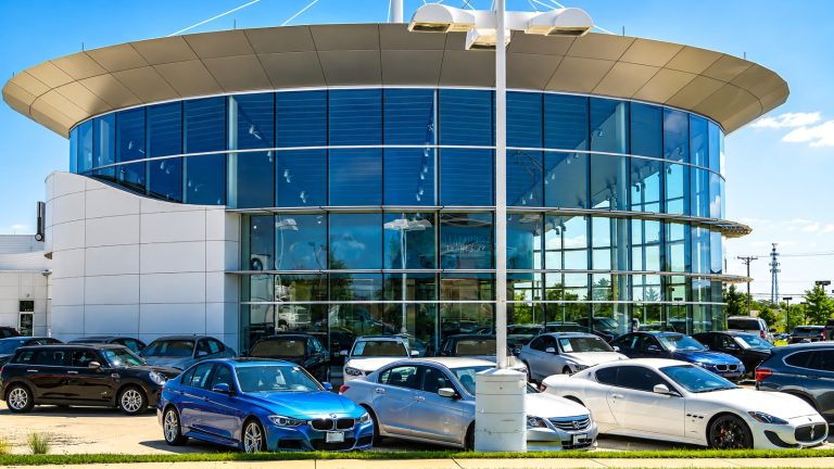 modern glass car dealership building with multiple cars parked in front