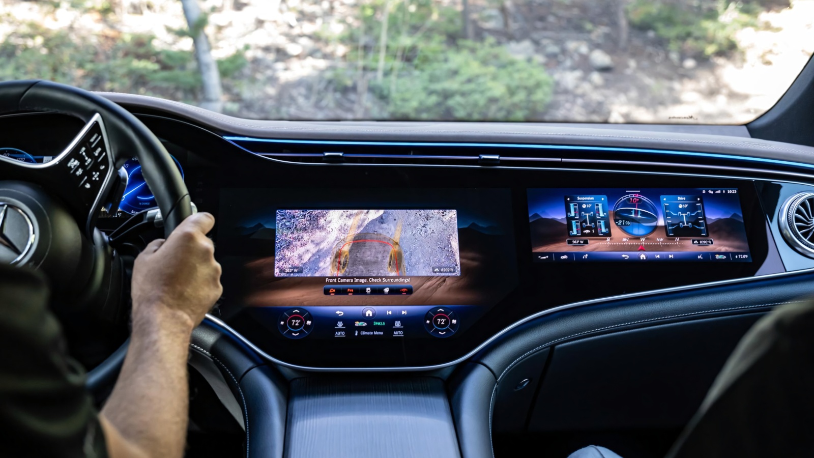A driver's hands on a steering wheel facing a wide digital dashboard with multiple screens