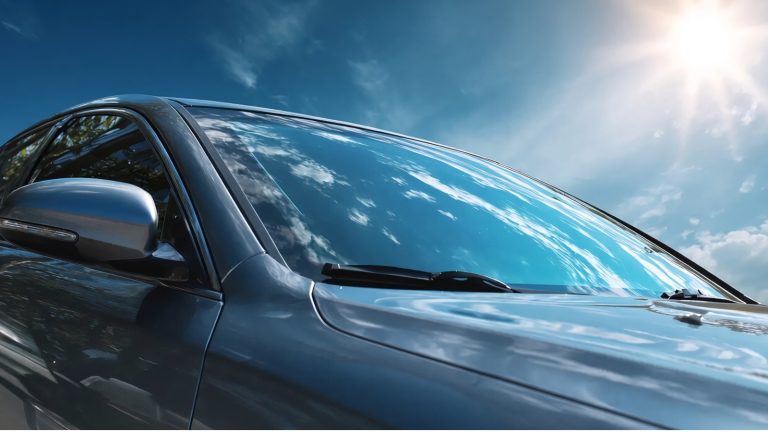 low-angle view of a dark car's windshield reflecting a bright, sunny sky