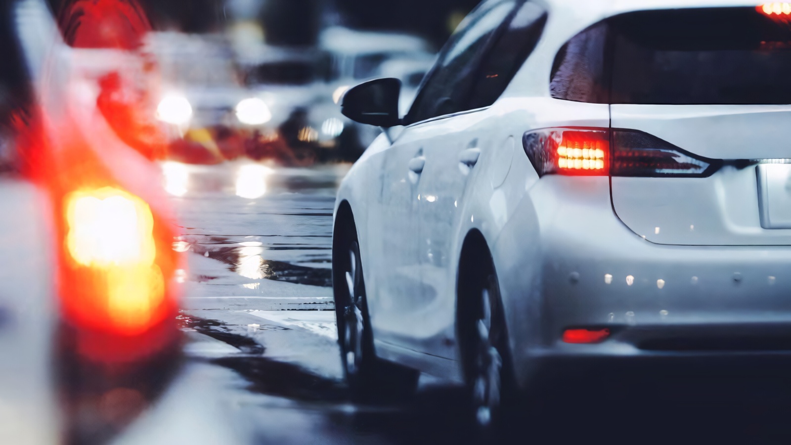 A white car driving in rainy evening traffic with bright glowing tail lights