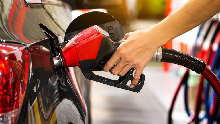 person's hand holding a red gas nozzle fueling a black car at a station