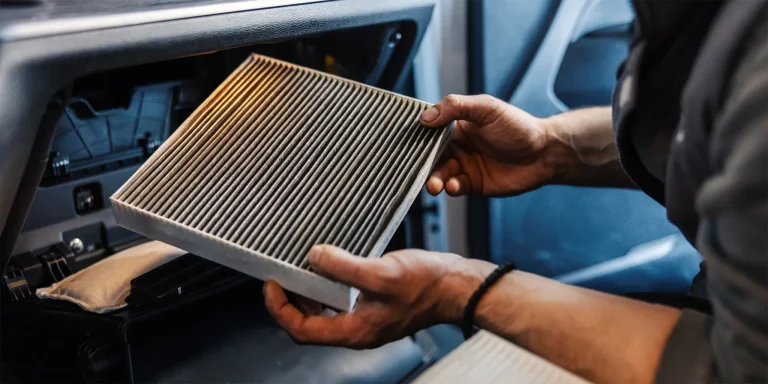 A pair of hands holds a dirty car cabin air filter inside a vehicle