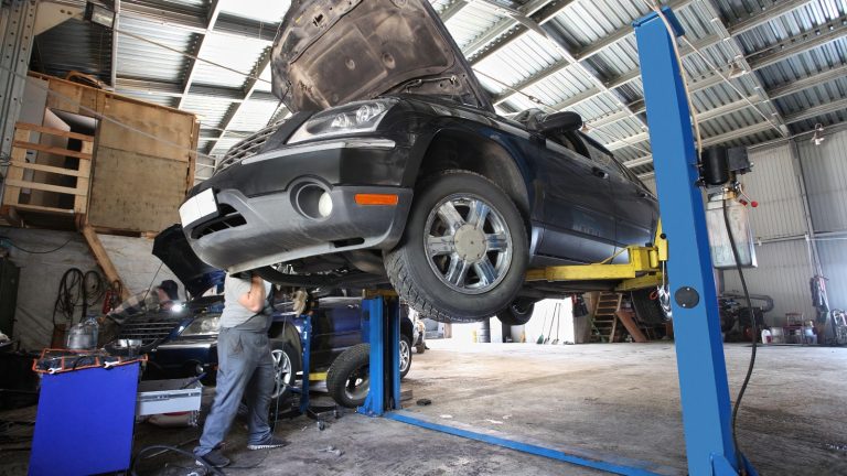 A mechanic works under a car elevated on a hydraulic lift in a repair shop