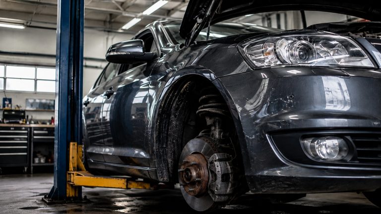 A dark car lifted on a hydraulic hoist in a mechanic's repair shop