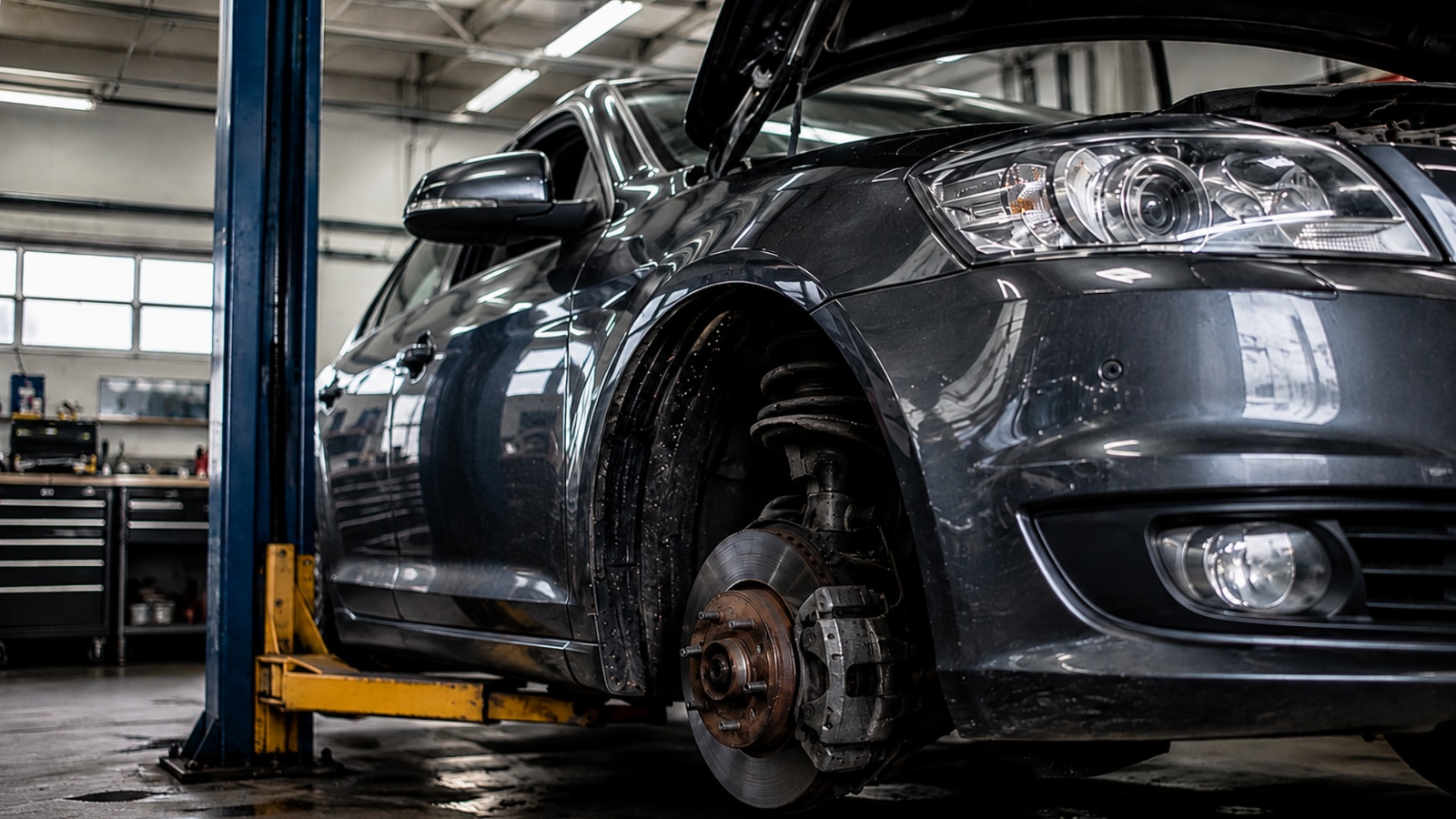A dark car lifted on a hydraulic hoist in a mechanic's repair shop