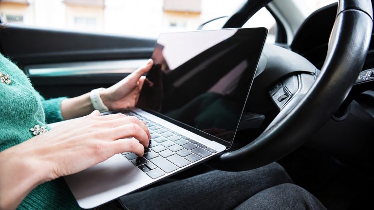 A person sitting in the driver's seat of a car while using a laptop