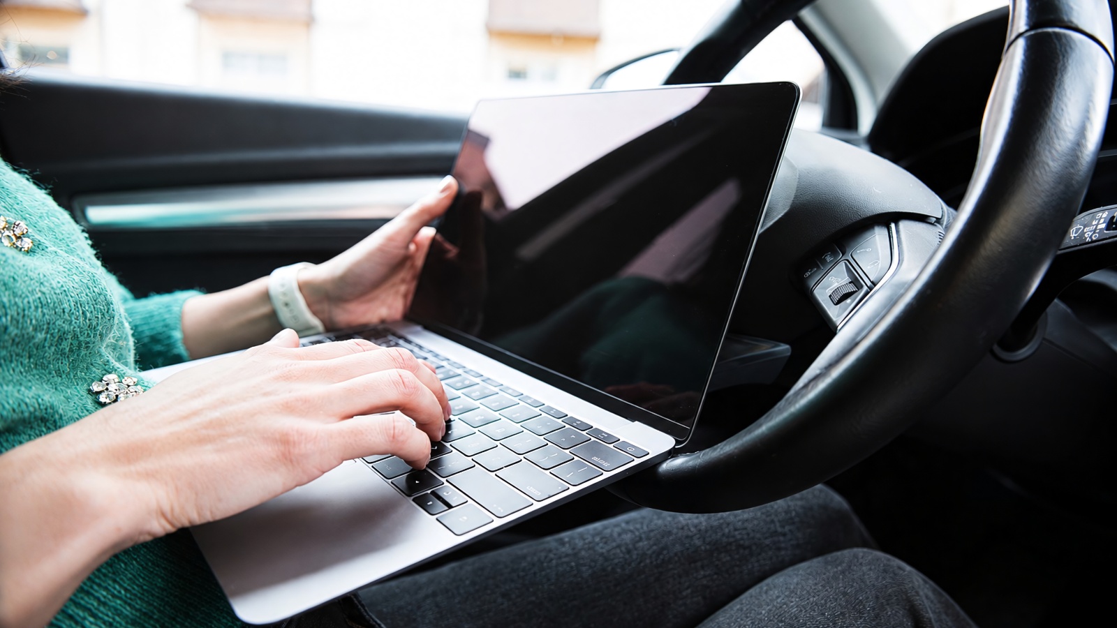 A person sitting in the driver's seat of a car while using a laptop