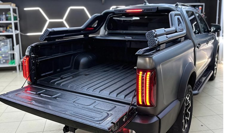 A dark gray pickup truck with an open tailgate and custom roll bar inside showroom