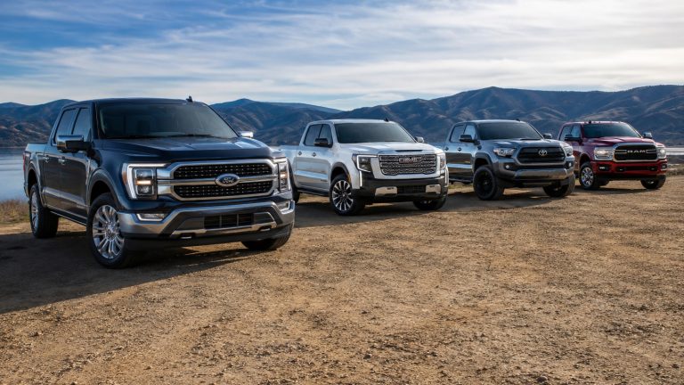 Four different pickup trucks parked in a row outdoors under a bright sky