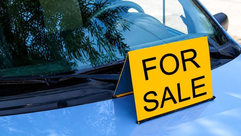 yellow "FOR SALE" sign sits on the hood of a blue car
