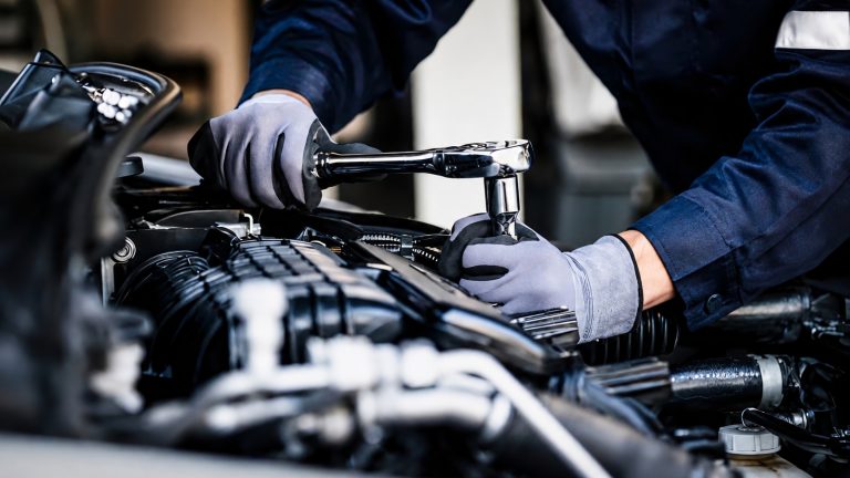 mechanic wearing gloves uses a ratchet to work on a car engine bay