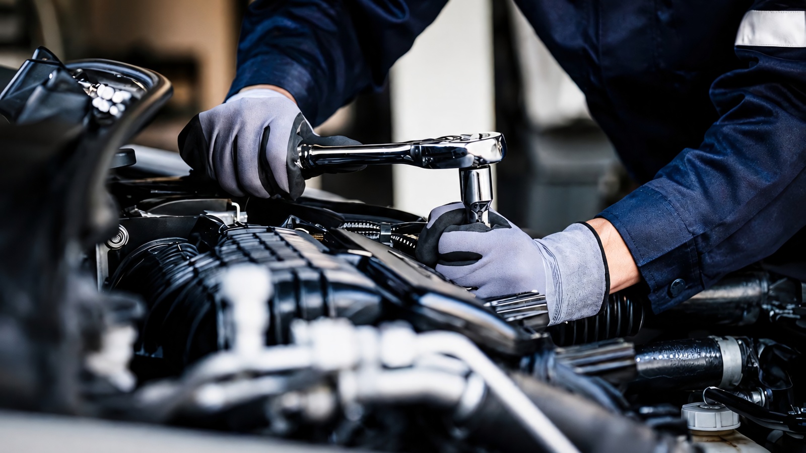 mechanic wearing gloves uses a ratchet to work on a car engine bay